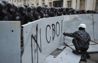 Участник акции пишет слово «Свобода» на металлическом заграждении перед отрядом «Беркута». 