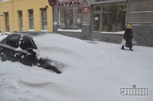 Прохожие идут возле занесенного снегом автомобиля на одной из улиц Львова