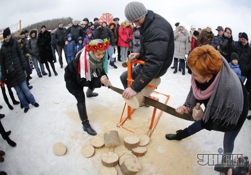 Участники празднования Масленицы распиливают бревно во время народных гуляний в национальном музее архитектуры и быта Украины