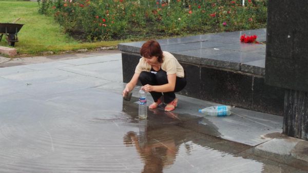 Женщина набирает дождевую воду в пластиковую бутылку