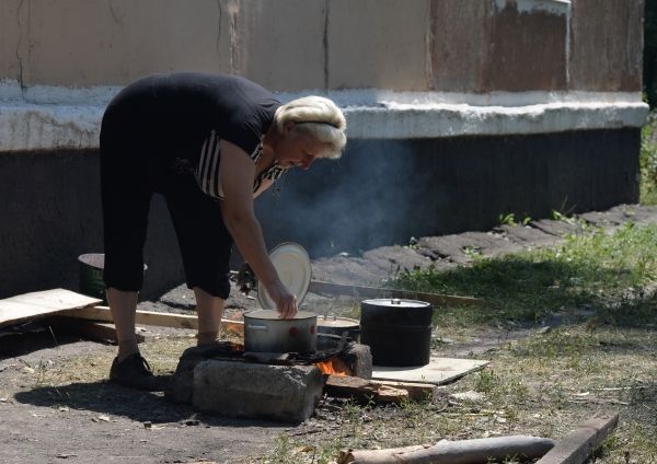 Жительница Шахтерска, лишившаяся дома, готовит еду рядом с подвальным убежищем.