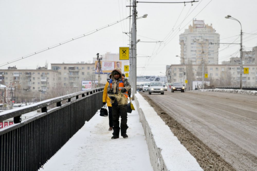 Дворник на Астраханском мосту посыпает пешеходную дорожку песком.