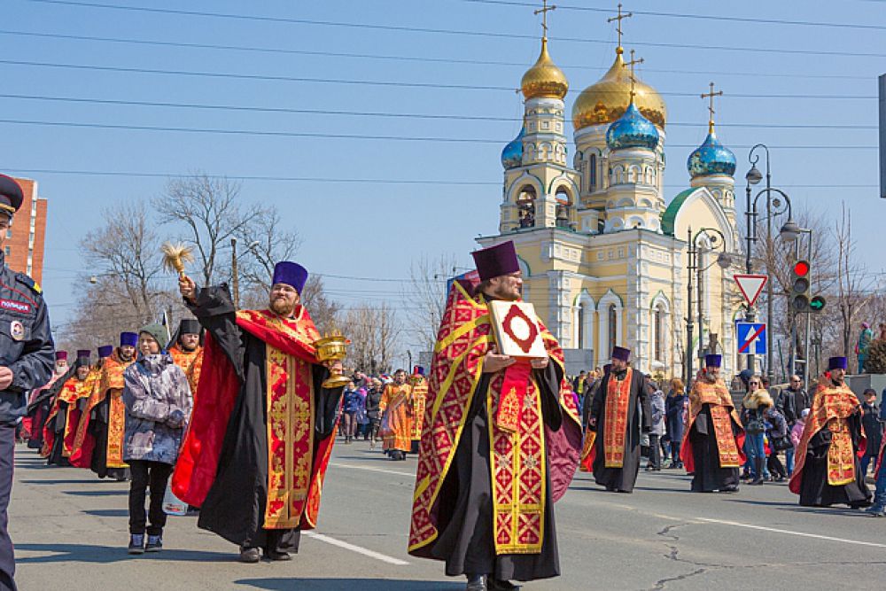 За ними священнослужители, окропляющие водой улицы и прохожих.