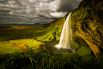 Водопад Селйяландсфосс, Исландия. Самый известный и живописный водопад Исландии. Это один из немногих водопадов, которые можно наблюдать «изнутри» — из скального грота за мощными потоками воды. Озеро, куда впадает Селйяландсфосс, окружают километры разноцветных полей, раскинутых под пронзительно голубым исландским небом.