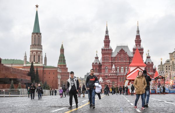  Туристы, несущие в руках теплые куртки, гуляют по Красной площади.