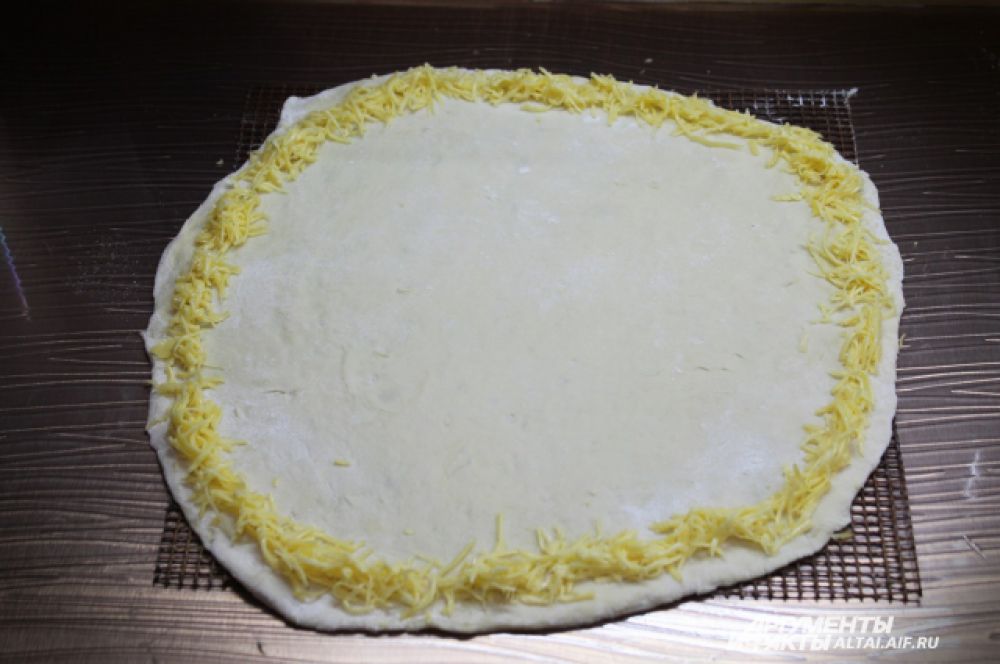 Тонко раскатываем тесто и сразу кладем его на противень или на специальную сетку для выпечки (как у меня). По краю выкладываем тертый сыр.