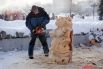 Художник рядом с снежными скульптурами выпилил из дерева медведей.