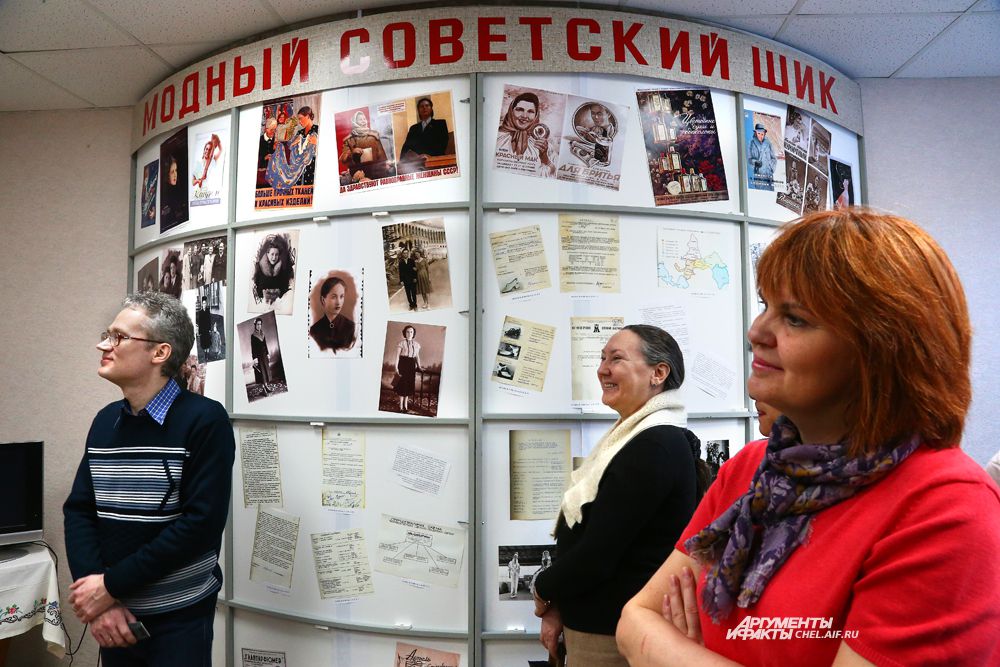 Посетители выставки на фоне банера с архивными документами и фотографиями.