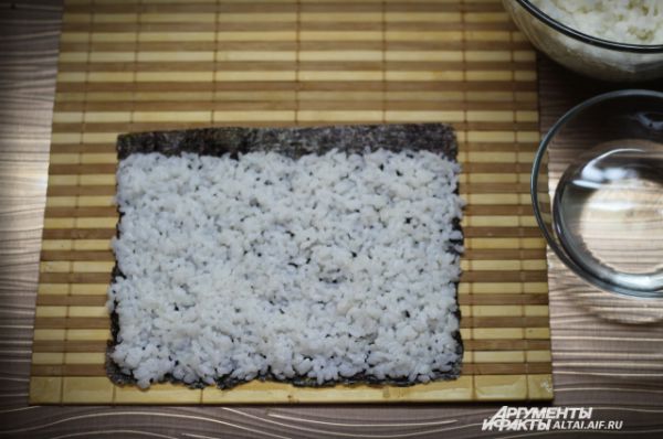 Равномерно выкладываем рис на нори, оставляем сверху полосу, примерно в один сантиметр без риса, для того чтобы ролл при сворачивании склеился. 