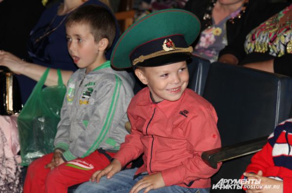Дети и внуки пограничников смотрят концерт в зеленых фуражках родственников.