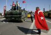 Человек, завернутый в турецкий флаг, проходит мимо военного автомобиля возле аэропорта Сабиха.