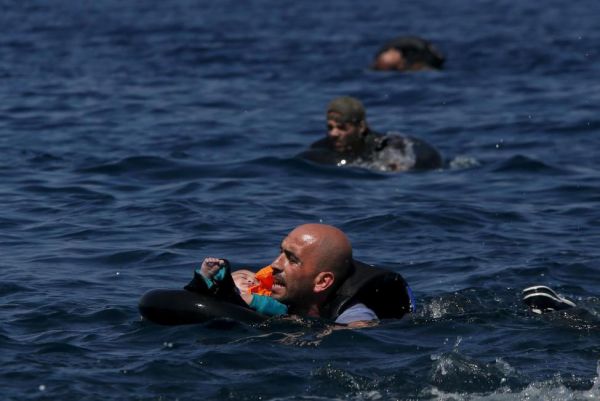 Сирийский беженец держит ребёнка в трубке, пытаясь доплыть к берегу после того, как их лодка потерпела крушение в 100 метрах от греческого острова Лесбос. Фото: Alkis Konstantinidis/ REUTERS, 13 сентября 2015 года.