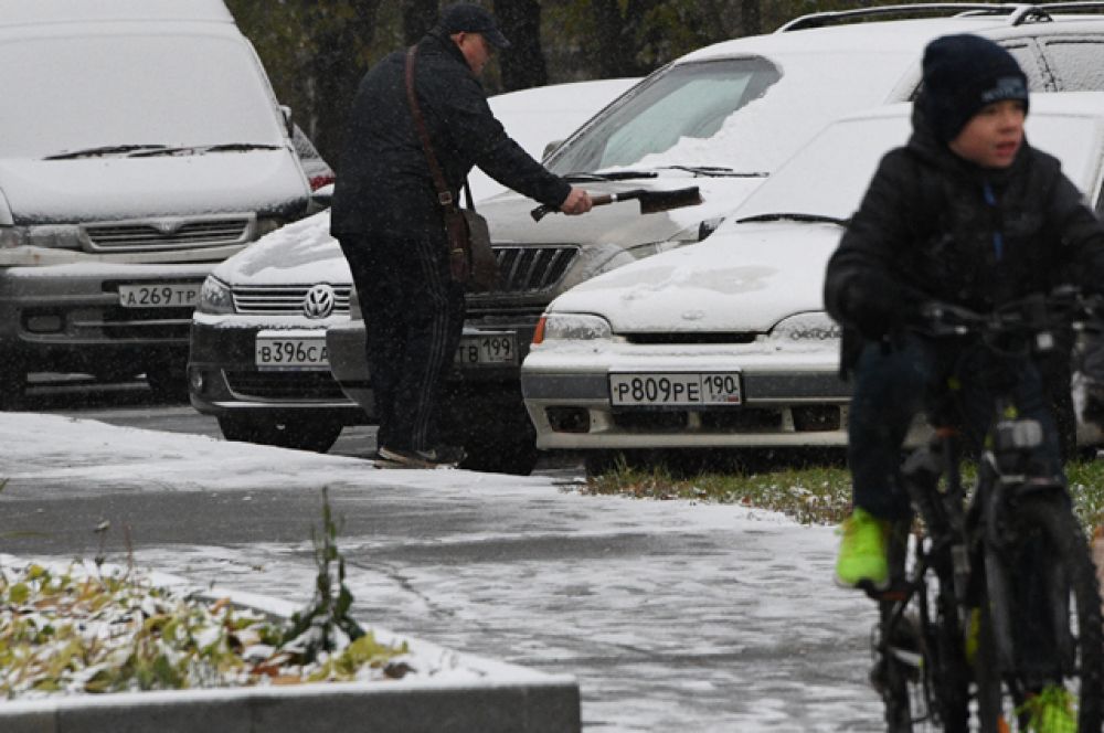 Мужчина очищает свой автомобиль от снега.