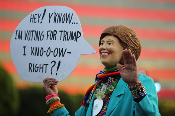 Человек в маске Хиллари Клинтон с плакатом «Знаете, я голосую за Трампа».