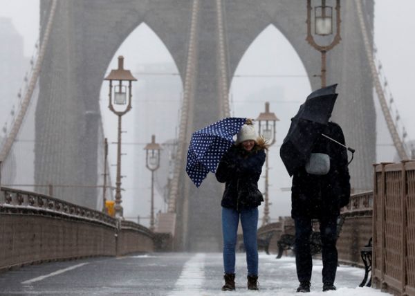 Люди борются с ветром и снегом на Бруклинскому мосту в Нью-Йорке.