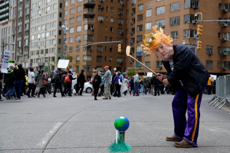 Участник акции в костюме Дональда Трампа, делает вид, что играет в гольф с Землей во время марша в защиту науки в Нью-Йорке.