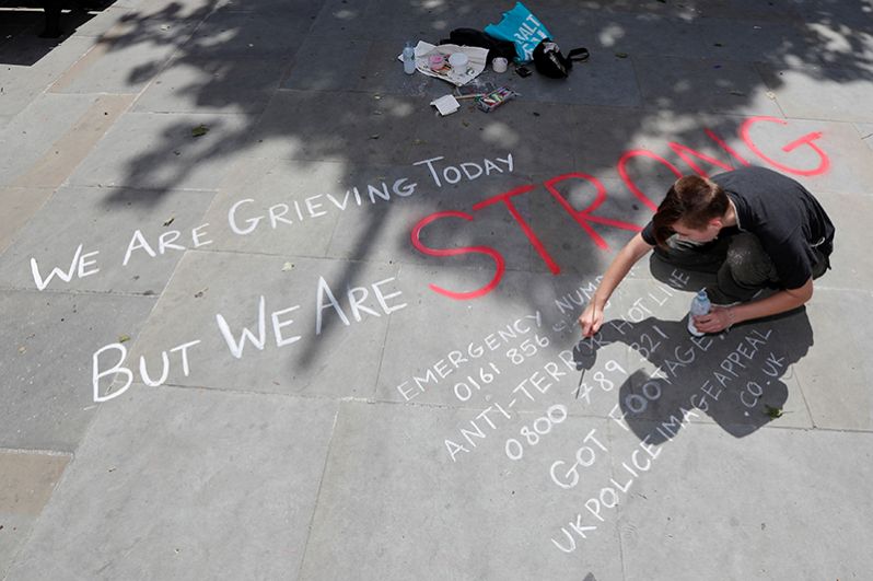 Мужчина пишет сообщение на тротуар в центре Манчестера: «Сегодня мы скорбим, но мы сильные».