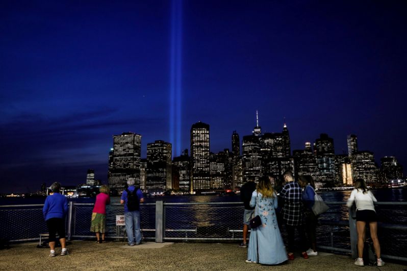 Люди смотрят на памятную инсталляцию «Посвящение в свете» — 88 направленных вверх прожекторов, создающих два мощных луча света.