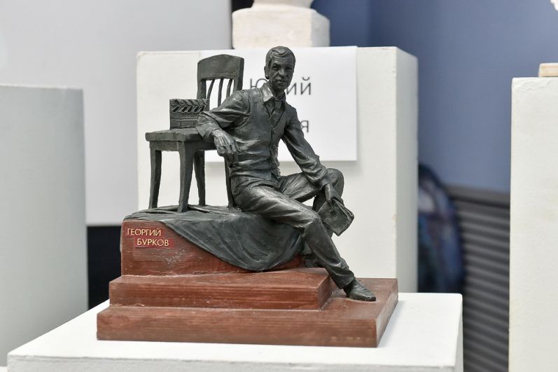 Юрий Злотя изобразил фигуру Георгия Буркова рядом со стулом с киношной хлопушкой.