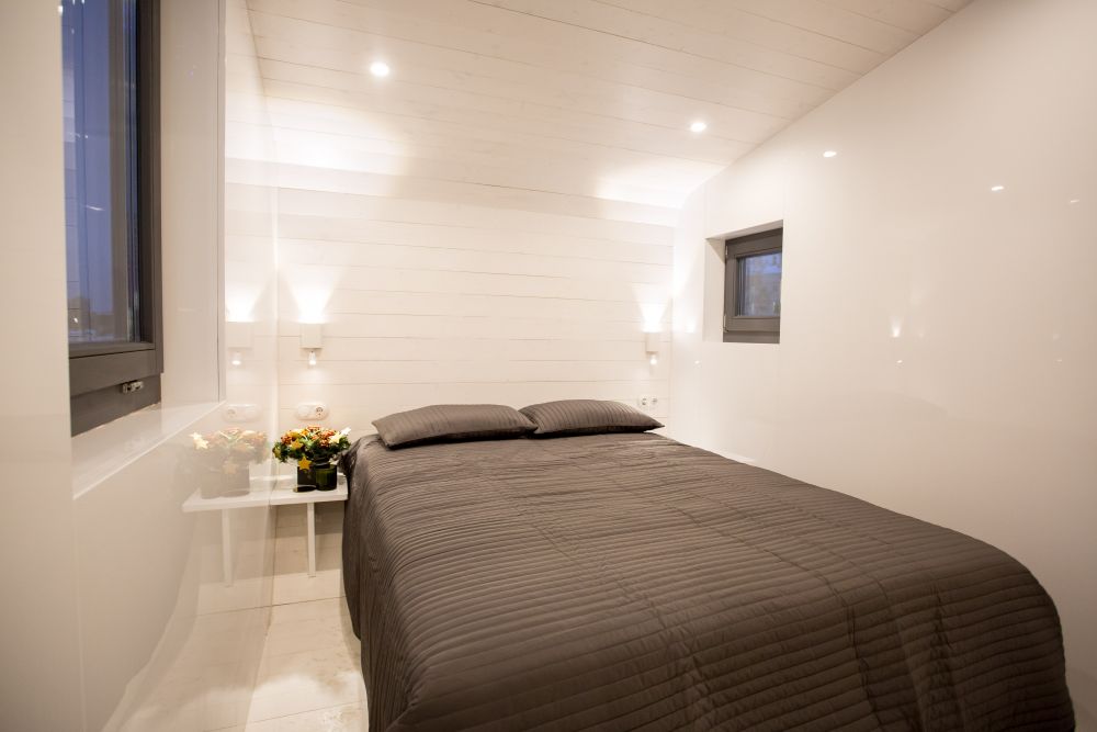 В мобильном туристическом доме площадью 19 кв. метров есть спальня с кроватью, встроенным шифоньером и столиками. 