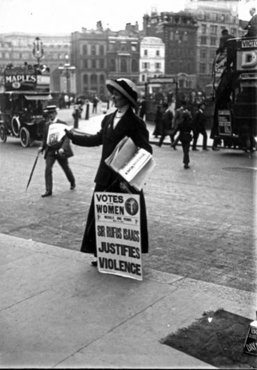 Британская суфражистка с плакатом раздает газеты или листовки на улице. Позади остановился двухъярусный автобус. Снято до 1919 года.