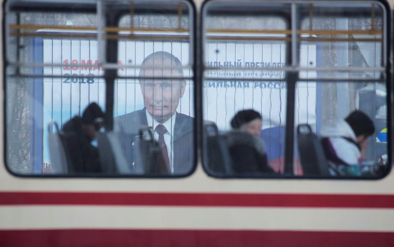 Люди едут на трамвае мимо рекламы президентской кампании Владимира Путина перед предстоящими выборами, Санкт-Петербург, Россия.