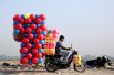 Мужчина с упаковками пластиковых шаров едет на своем мотоцикле в Дели, Индия.