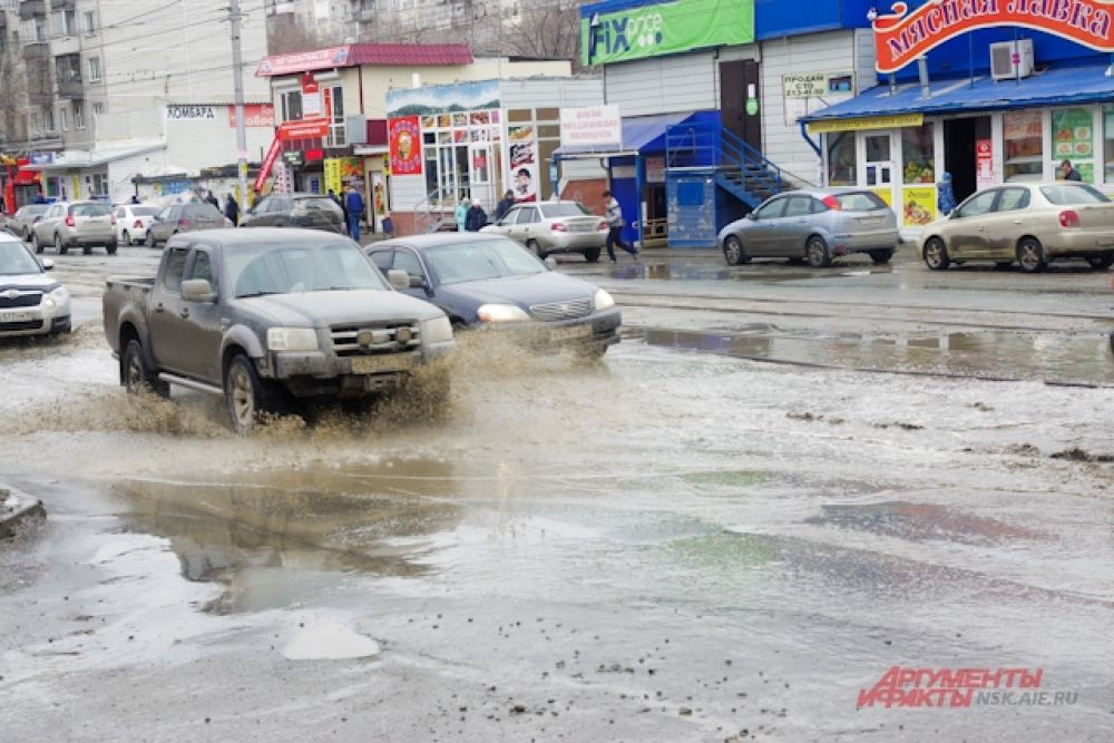 Машины проезжают по дороге, а вода из лужи разливается на несколько метров.