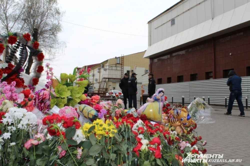 Люди продолжают нести к стихийному мемориалу возле сгоревшего ТЦ цветы и игрушки.