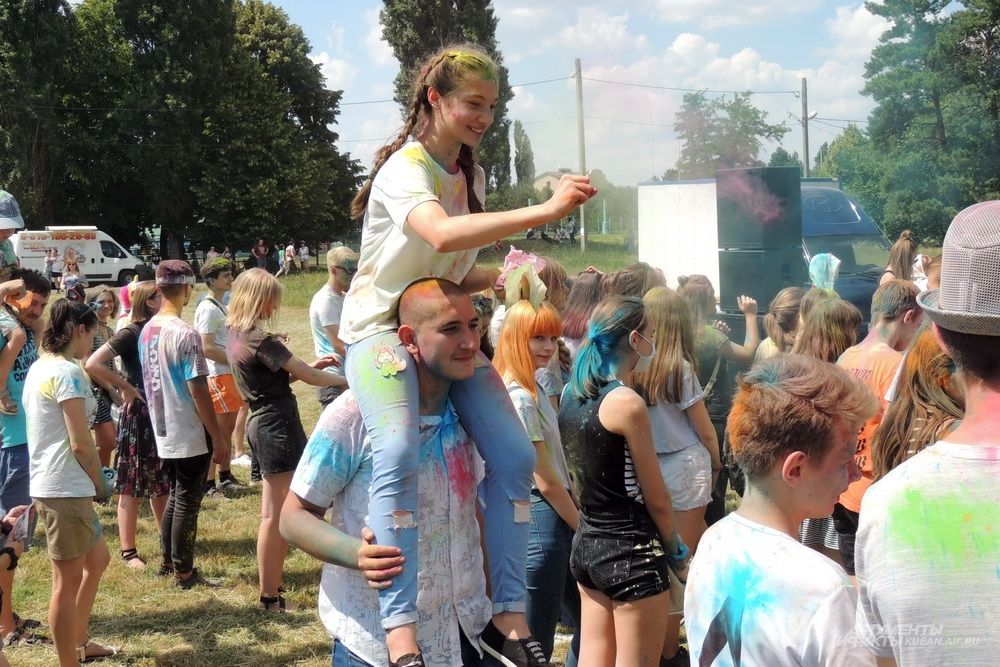 Девушка обсыпает участников фестиваля краской, сидя на шее у парня.