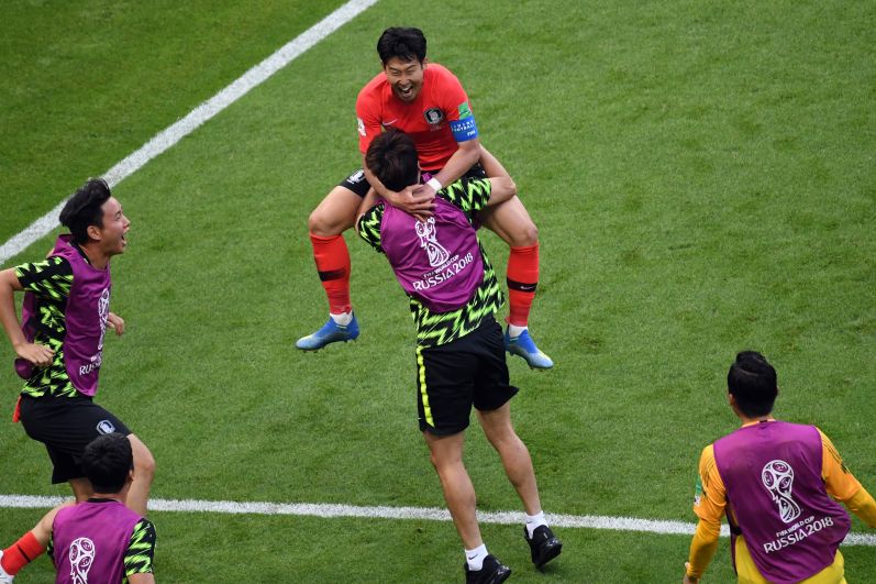 Сон Хын Мин, забивший второй гол, в восторге прыгает на плечи товарищу по команде.