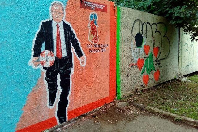 На граффити Президент России, изображённый в костюме, наносит удар по мячу. 