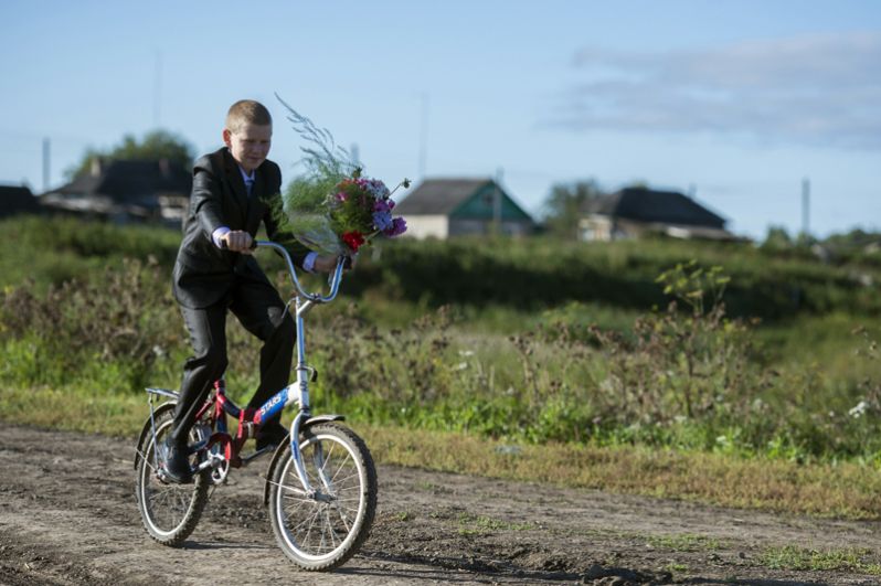 Мальчик с цветами едет в школу в селе Кирилино Омской области.