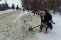 Местная «Агафья Лыкова» расчищает подход от дороги к своему дому двумя лопатами.