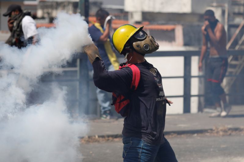 Демонстрант бросает гранату со слезоточивым газом во время акции протеста против правительства Николаса Мадуро.