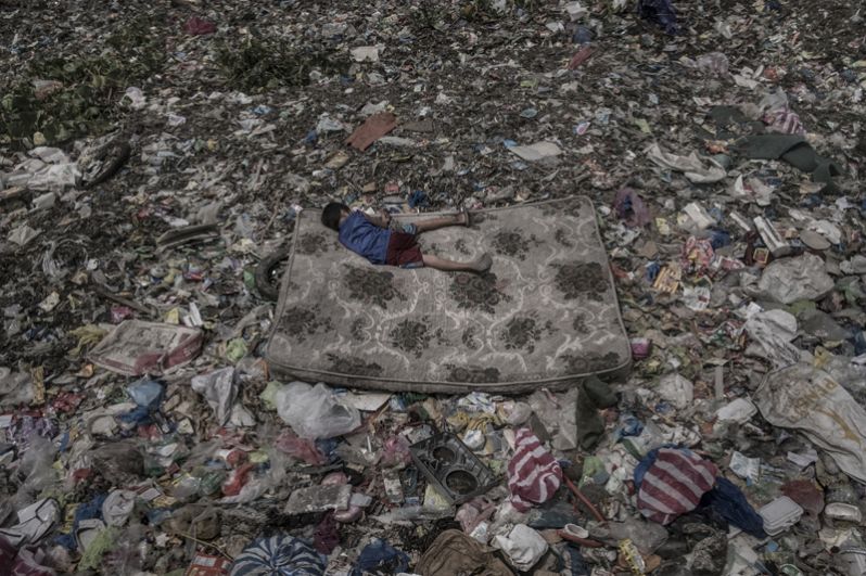 Ребенок лежит на матрасе, окруженном мусором, плавающим в реке Пасиг в Маниле, Филиппины.