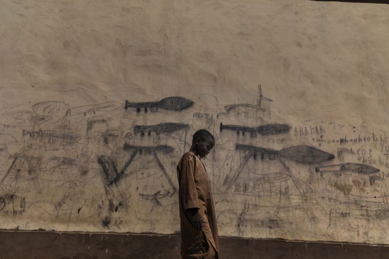 Мальчик-сирота проходит мимо стены с рисунками гранатометов в Боле, Чад.