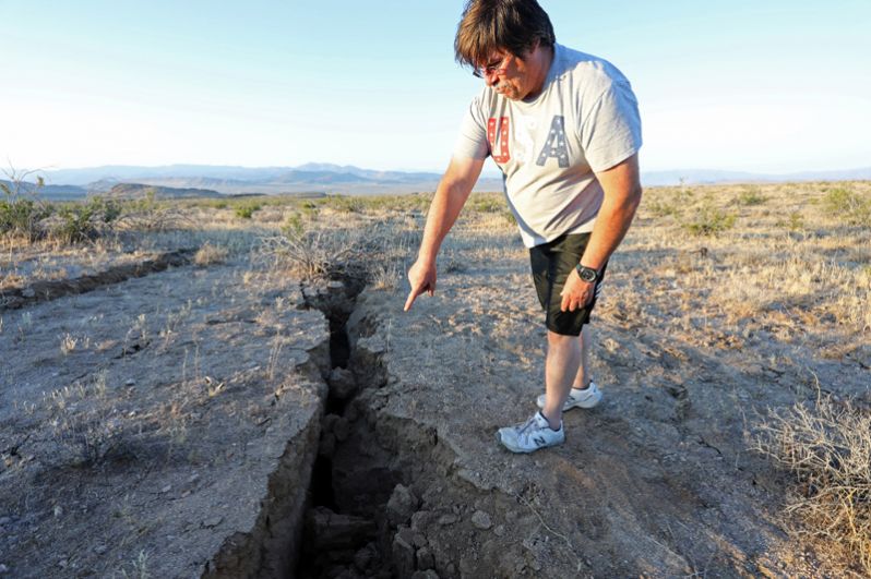 Мужчина показывает трещину, образовавшуюся в результате землетрясения.