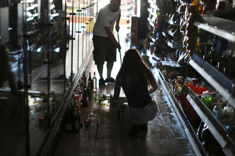 Люди убирают разбитые бутылки в винном магазине после мощного землетрясения в городе Риджкрест.