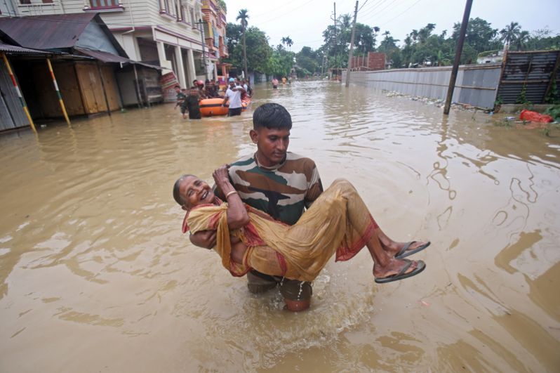 Мужчина несет пожилую женщину в безопасное место после проливных дождей в деревне Балдахал, на окраине города Агартала.
