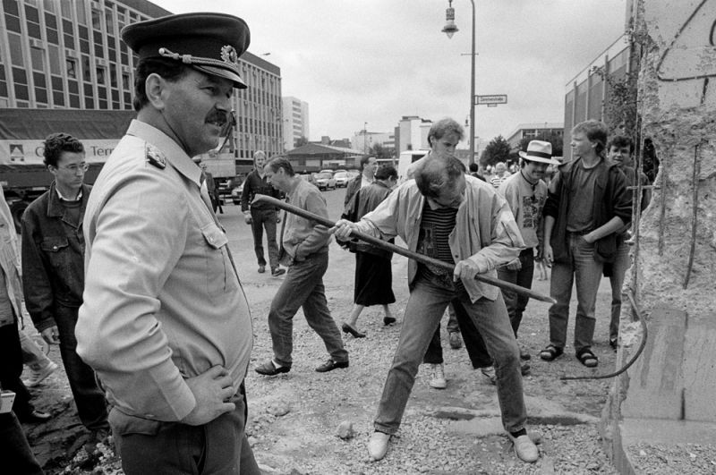 Пограничник смотрит на мужчину, который откалывает кусок Берлинской стены на Руди-Дутшке-штрассе.