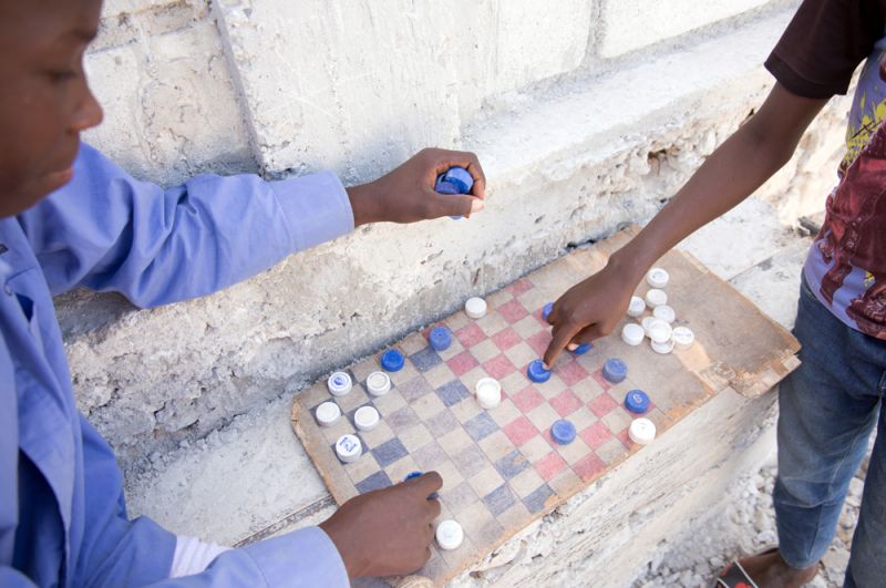 Дети играют в шашки пластиковыми крышками для бутылок.