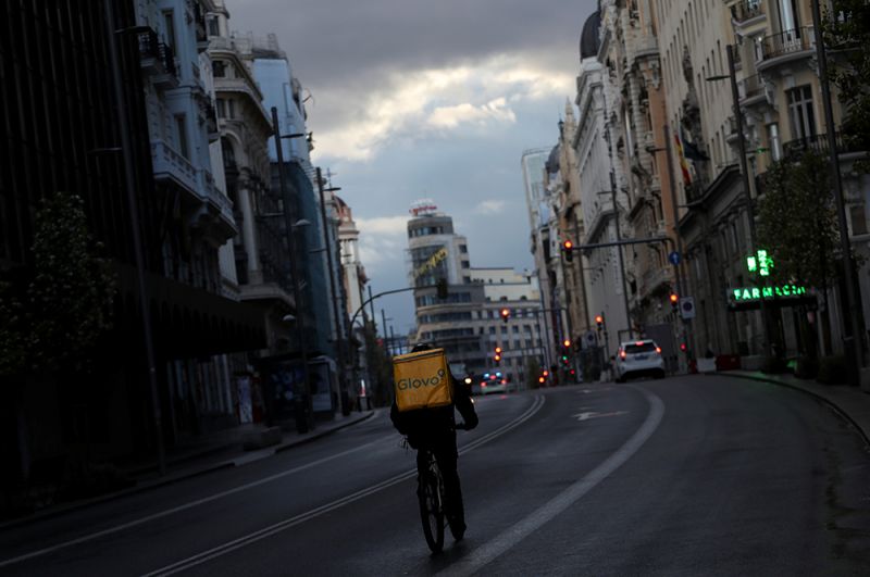 Сотрудник службы доставки едет на велосипеде по пустой улице Гран Вия в Мадриде.