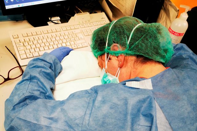 Медсестра, уснувшая за столом после ночной смены в больнице Кремоны, Италия.