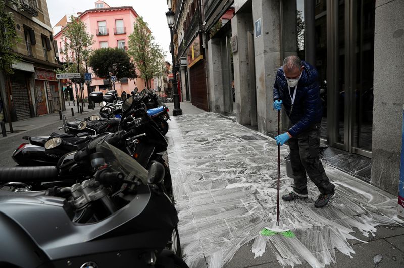 Владелец отеля, закрытого из-за вспышки коронавируса, моет тротуар перед ним, Мадрид.