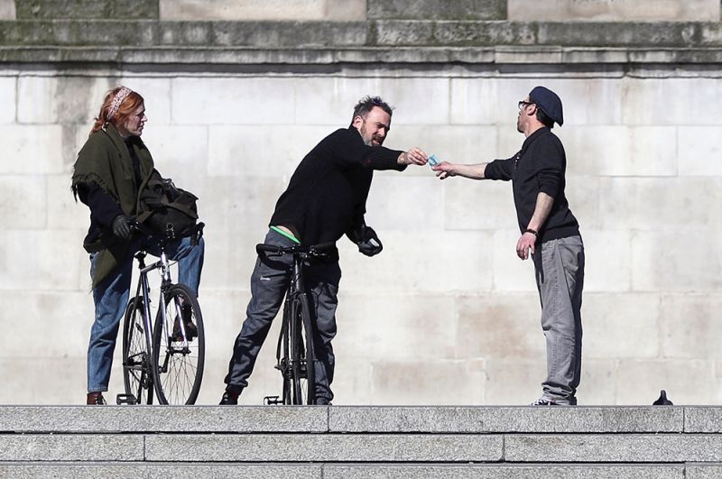 Мужчины держат дистанцию, передавая деньги друг другу, Трафальгарская площадь, Лондон.
