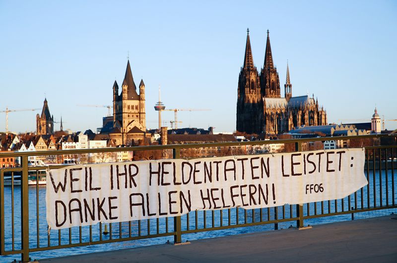 Плакат с надписью: «Потому что вы совершаете героические поступки, спасибо всем, кто помогает» на мосту перед Кельнским собором, Кельн, Германия.