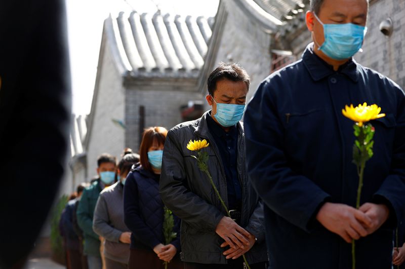 Местные жители с цветами в руках во время минуты молчания в Пекине.