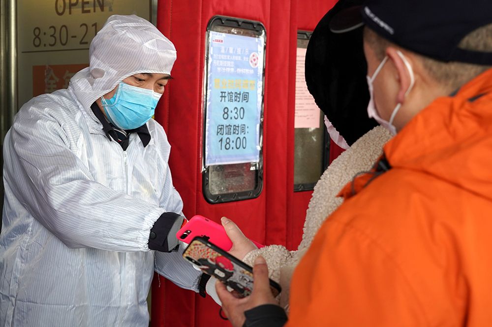 Сотрудник сканирует QR-коды жителей у входа в супермаркет в Чжэнчжоу.