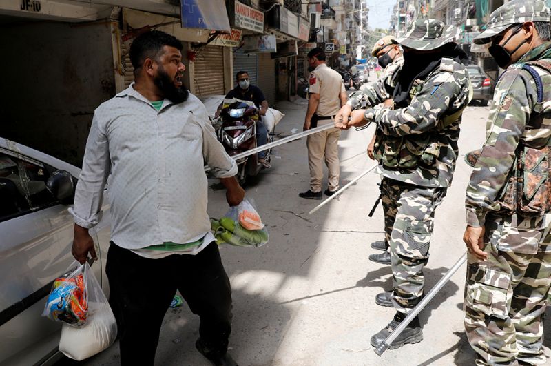 Полицейские применяют дубинки против мужчины, нарушившего режим, Нью-Дели, Индия.